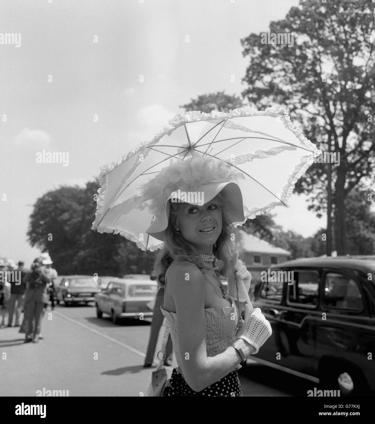 Sally Farmiloe chose a brief cotton top over a polka dot skirt for Ladies Day at Royal Ascot. The outfit was complimented with a feather trimmed hat and parasol. Stock Photo