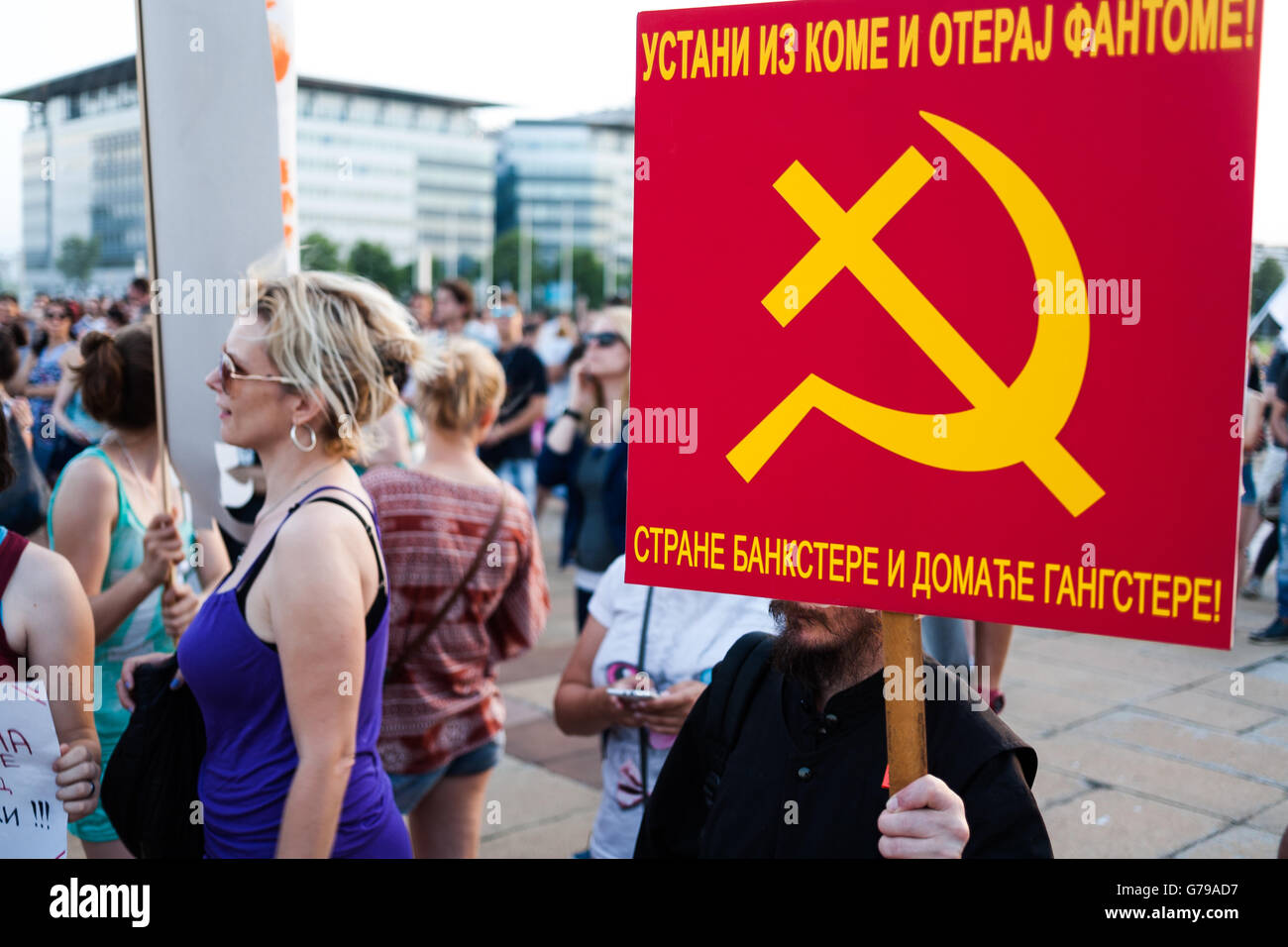 Belgrade, Serbia. 25th June, 2016. Demonstrator in front of Palace of Serbia with crossing cross and sickle banner. It captioned 'Raise from coma and get rid of phantoms'. Milos Bojovic/Alamy Live News Stock Photo