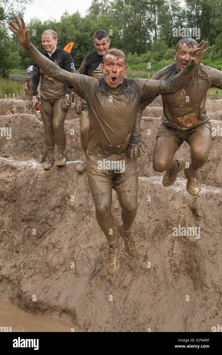 Tough Mudder mucky mad men jumping into muddy bath on the Mud Mile obstacle wet muddy obstacle course at Drumlanrig Castle, Dumfries and Galloway, Scotland, UK. Stock Photo