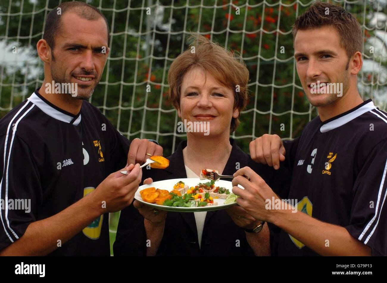 Norwich City Football Club Director Delia Smith is sandwiched between Norwich City players Adam Drury (right, Captain) and Craig Fleming (left, Club Captain) at the Norwich City training ground in Norwich. The celebrity chef and club shareholder shows off a plate of food that forms part of her Fuel Time Plan, a carbohydrate-rich, low-fat eating strategy for the team. Stock Photo