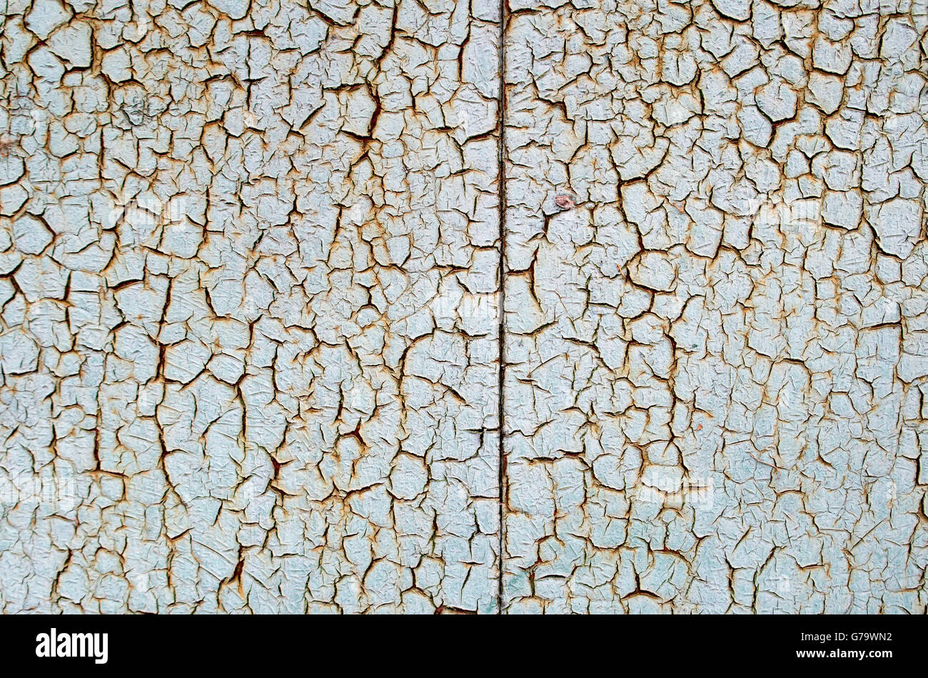 Rusty metal surface is covered with a thick layer of paint which has cracked from age to use as a background. Stock Photo