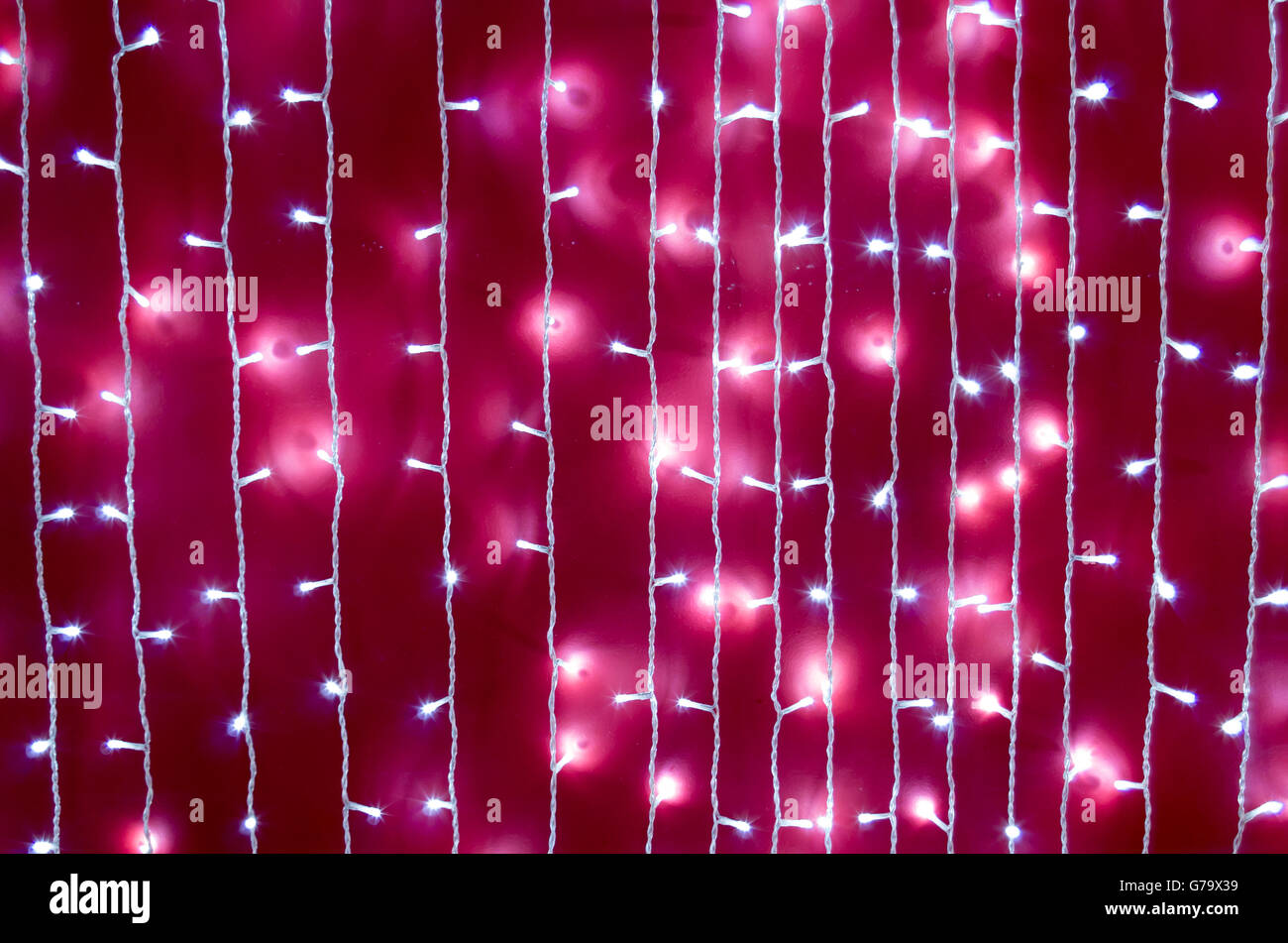 Defocused and blurred image of a bright red wall with white lights on the white wires vertical rows. Stock Photo