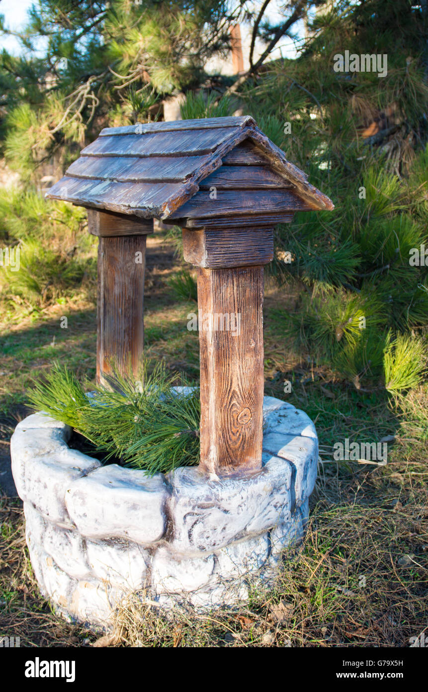 Decorative stone well in the park with a wooden roof and pine branches ...