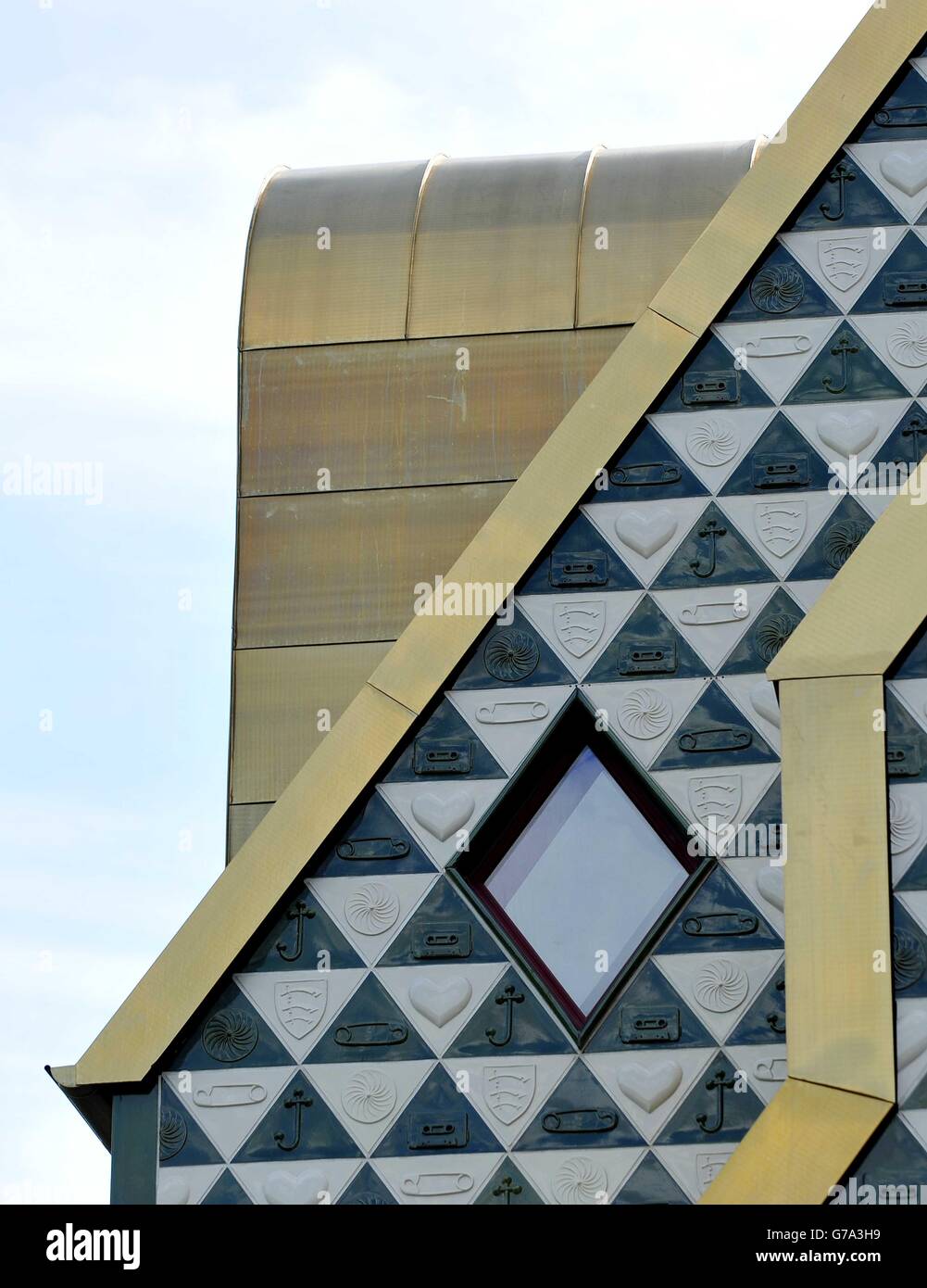 A view of the gold coloured structure and of tiles showing a cassette tape, the Essex Coat of Arms, a safety pin, a heart, a wheel pattern and a crossed hook, on the outside of 'Home for Essex' a new art project by artist Grayson Perry, under construction in Wrabness, Essex. Stock Photo