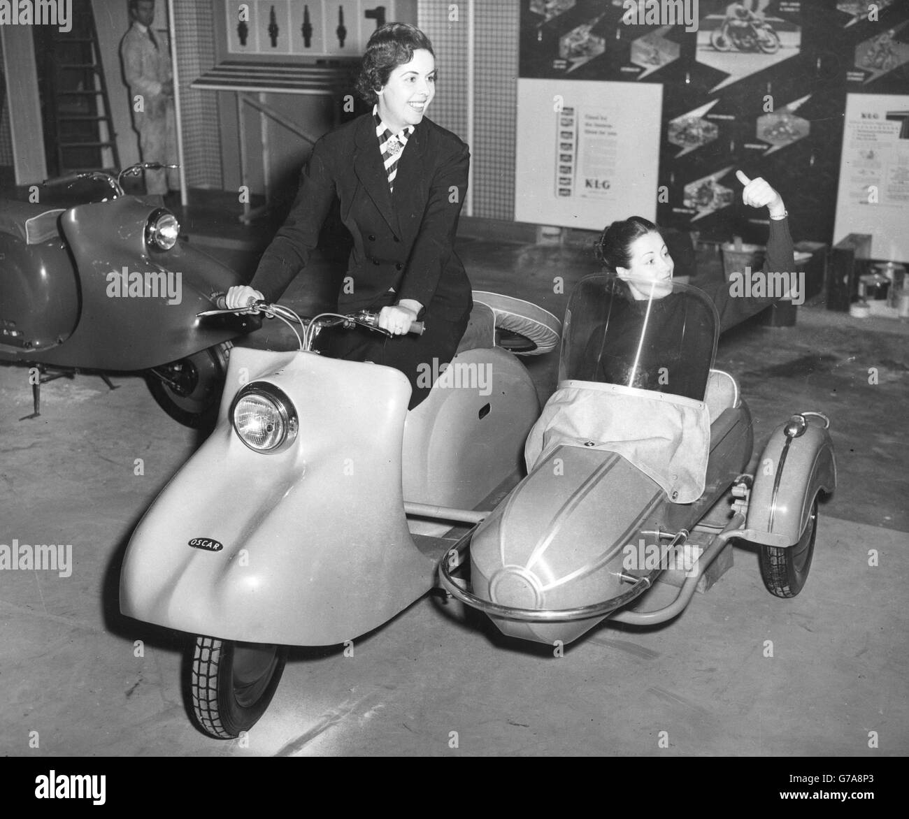 Smoothly streamlined and with a sidecar to match is the 197cc Oscar, a new British motor-scooter, which is being exhibited in Britain for the first at the Cycle and Motorcycle Show, opening at Earls Court, London. Trying out the combination at Earls Court are Jean Street (l) and Anne Long. The machine, powered by a two-stroke Villiers engine, can carry two people on a duel seat and also has space for two suitcases. *Scan from print. Hi-res version available on request. Stock Photo