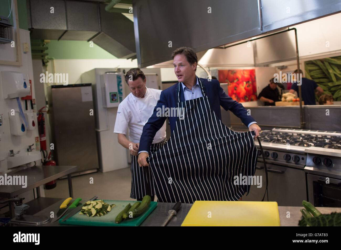 Deputy Prime Minister Nick Clegg puts on an apron with the help of Mark Stower, Director of Food and Service, Harrison Catering Services, during a visit to Clapham Manor Primary School in south west London, where he officially launched the government's scheme to provide 5-7 year olds with free school meals. Stock Photo