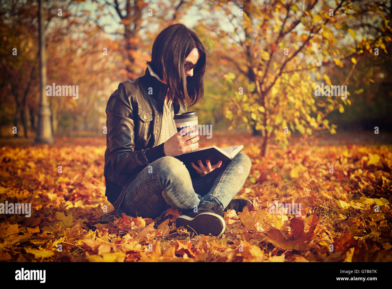 girl with coffee cup reading a book, sitting on leaves. Vintage photo Stock Photo