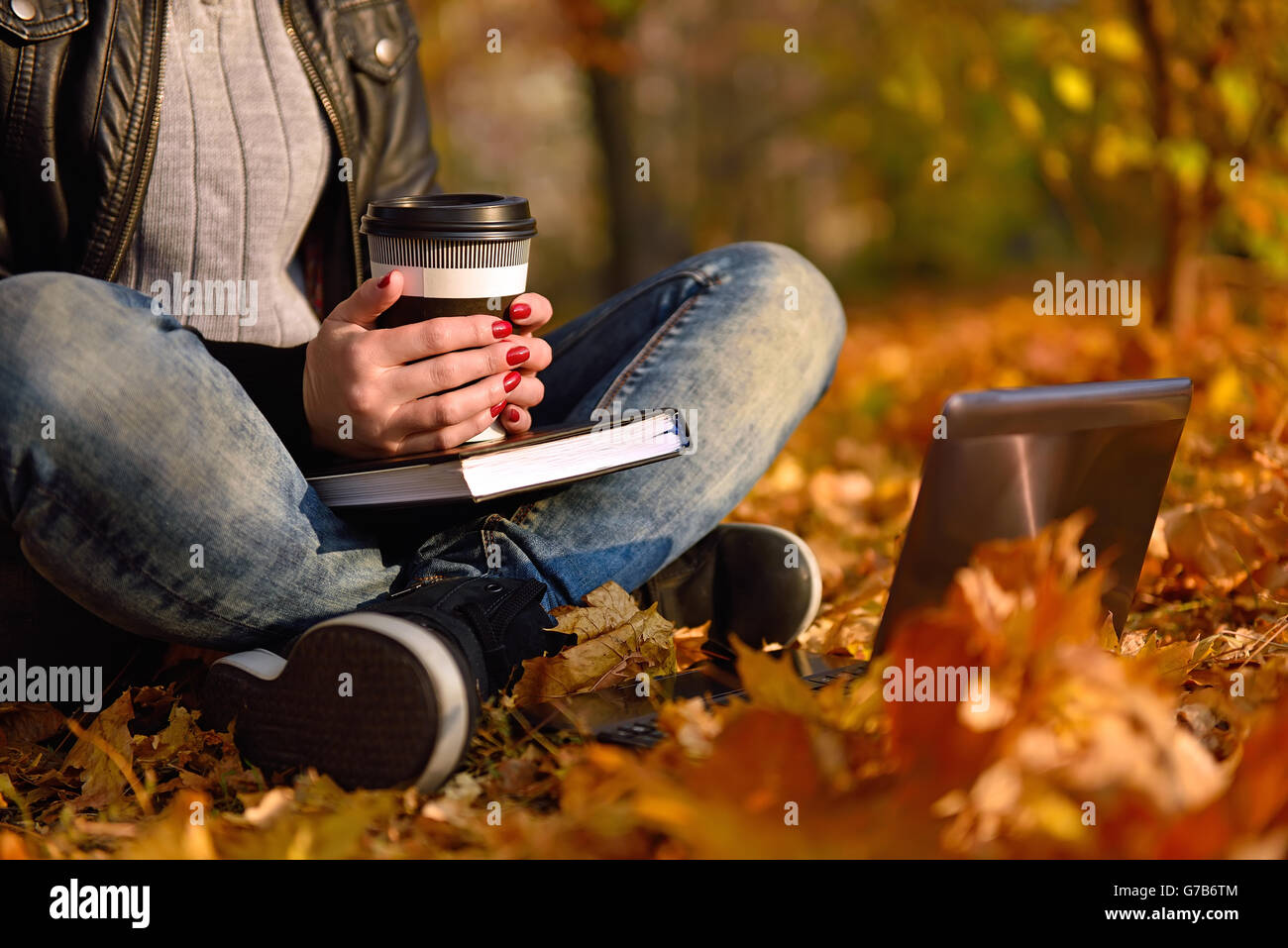 girl with coffee cup sitting on leaves in park. Vintage photo Stock Photo