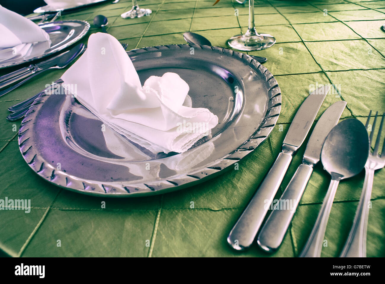 Photograph of some silver cutlery and a plate with a napkin, on a green