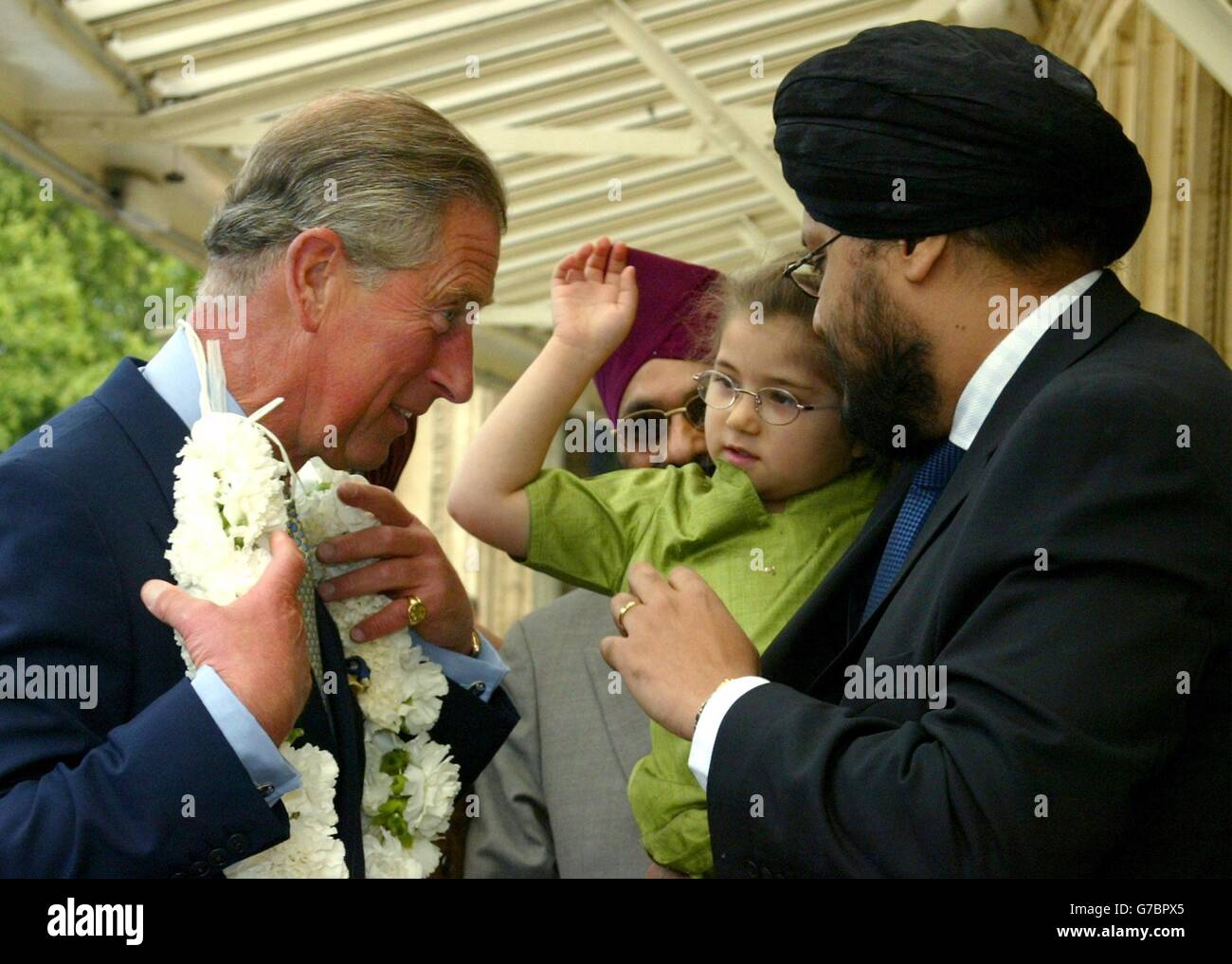 Britain's Prince Charles (left) is presented with a haar by 4-year-old Tauleen, as she is held by her father Dr Balwinder Singh (right), as he arrives for a celebration of the 400th anniversary of the first reading of the Guru Granth Sahib Sikh Scriptures at the Royal Albert Hall in London. The event was organised by the Network of Sikh Organisations to commemorate the 400th year of the Sikh holy book, the Guru Granth Sahib, a collection of the verses of the Sikh Gurus. Stock Photo