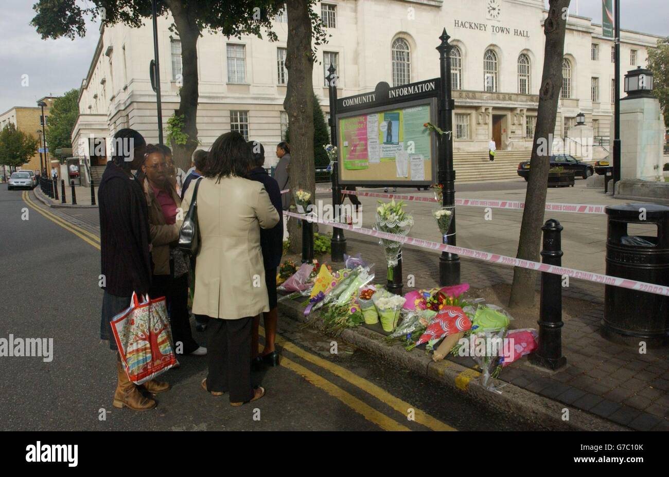 Locals gather near flowers, for an as yet unnamed 16 year old schoolboy who was stabbed to death near Hackney Town Hall, London. The boy was stabbed during the clash in east London, shortly before 4pm yesterday as school classes finished. Witnesses said they saw youngsters chasing each other along Mare Street before the fatal wounding. Stock Photo
