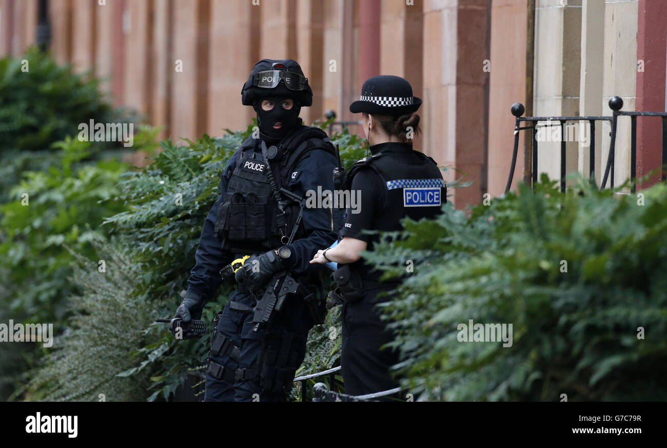 An armed police officer speaks to another officer near to the scene in Boyd Street in the Crosshill area of Glasgow, after police were called to an incident. Stock Photo