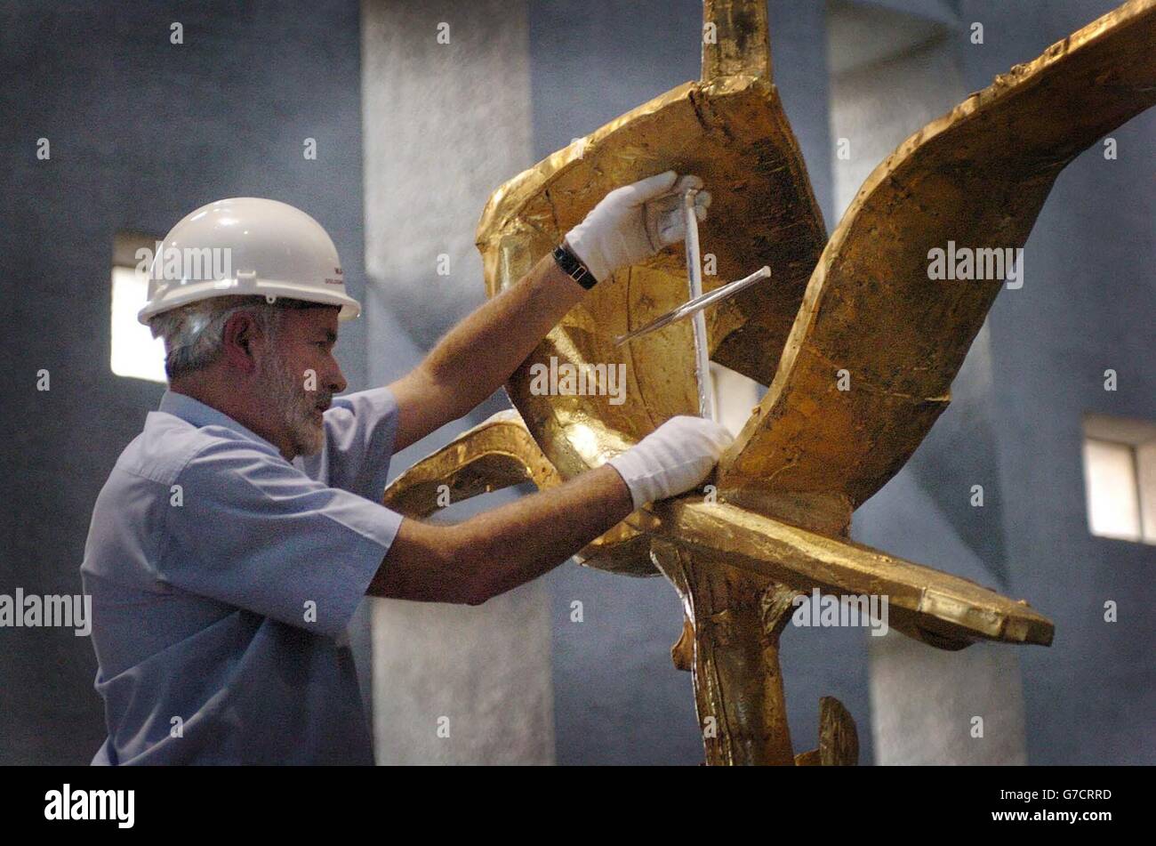 Grant Macdonald finally unwraps the 'Cross of Nails' as it is reinstalled at Coventry Cathedral. A team of silversmiths have laboured for 12 hrs a day for the last six weeks to clean and re gild the Geoffrey Clark sculpture using 2 kilos of 24 carat gold for the final surface. The cross reinstalled this weekend will is to be unveiled to the public at a special service today. Stock Photo