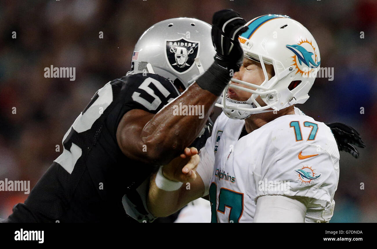 Miami Dolphins quarterback Ryan Tannehill (right) receives a blow to the helmet from Oakland Raiders Khalil Mack (left) during the NFL International Series 2014 match at Wembley Stadium, London. Stock Photo