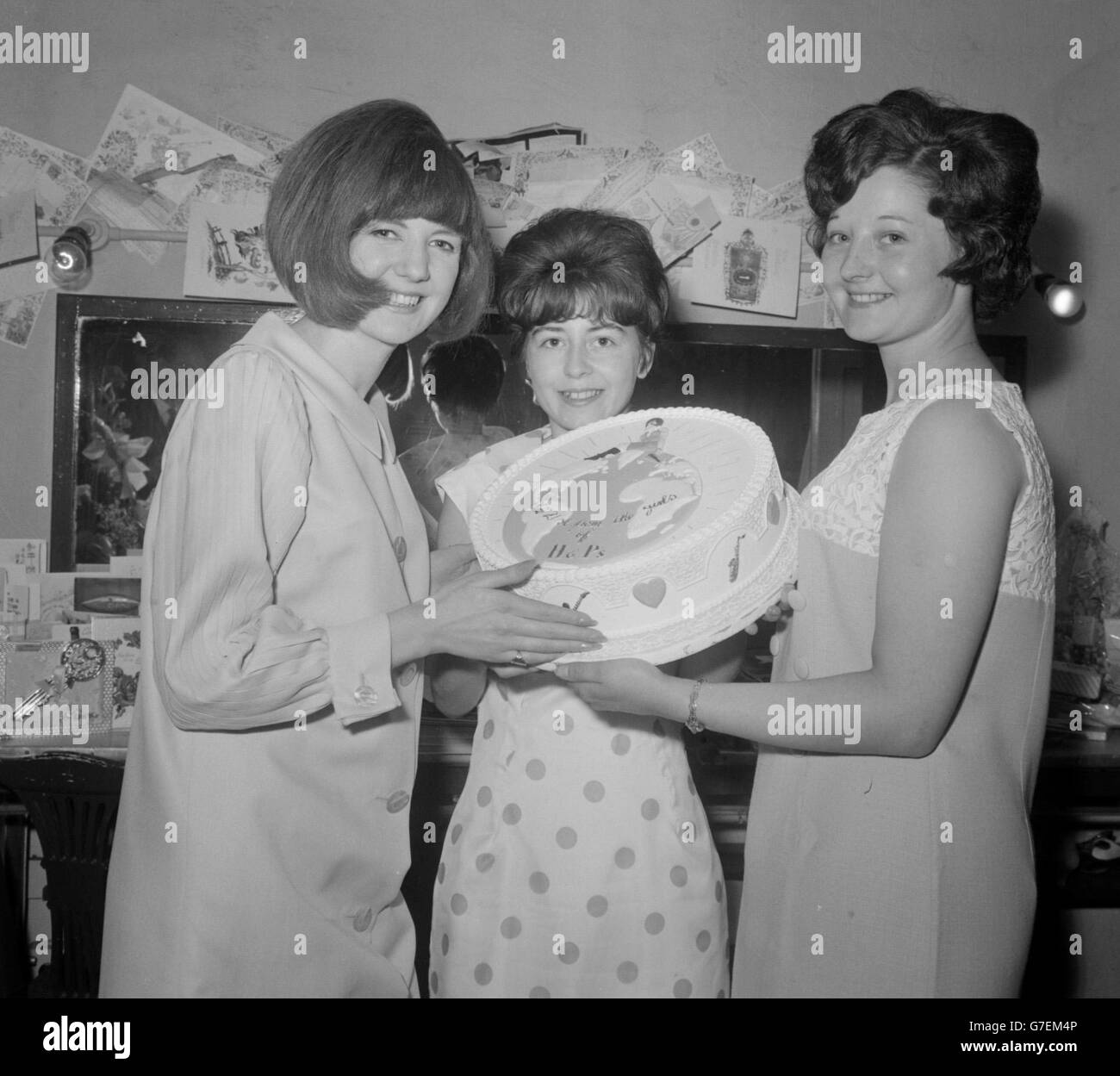 Top of the pops star Cilla Black (left) whose 'You're My World' record has gone to the top of the hit parade this week, pictured when she received a special 'on top of the world' cake from Pamela Yates, 21 (right) of Rainhill, Liverpool, and Mavis Moorcroft, 16, also of Rainhill, backstage at the London Palladium on Cilla's 21st birthday. Stock Photo