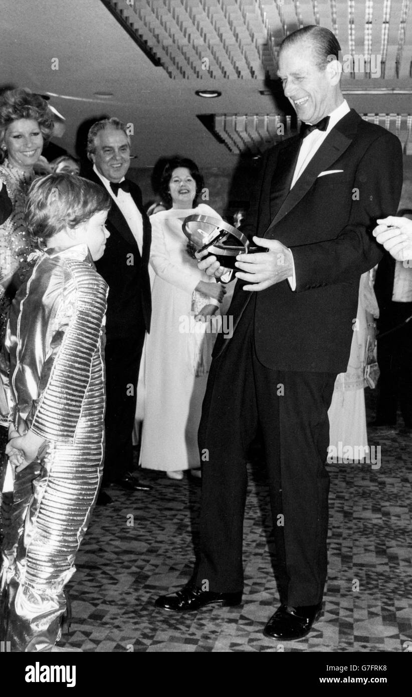 A model of astronaut apparatus is handed to an amused Duke of Edinburgh by space-suited seven-year-old Sascha Auerback, at the Odeon, Leicester Square, London, just before the Royal World Charity Premiere of the latest 007 Bond film, 'Moonraker'. *Scanned low-res from print, high-res available on request* Stock Photo