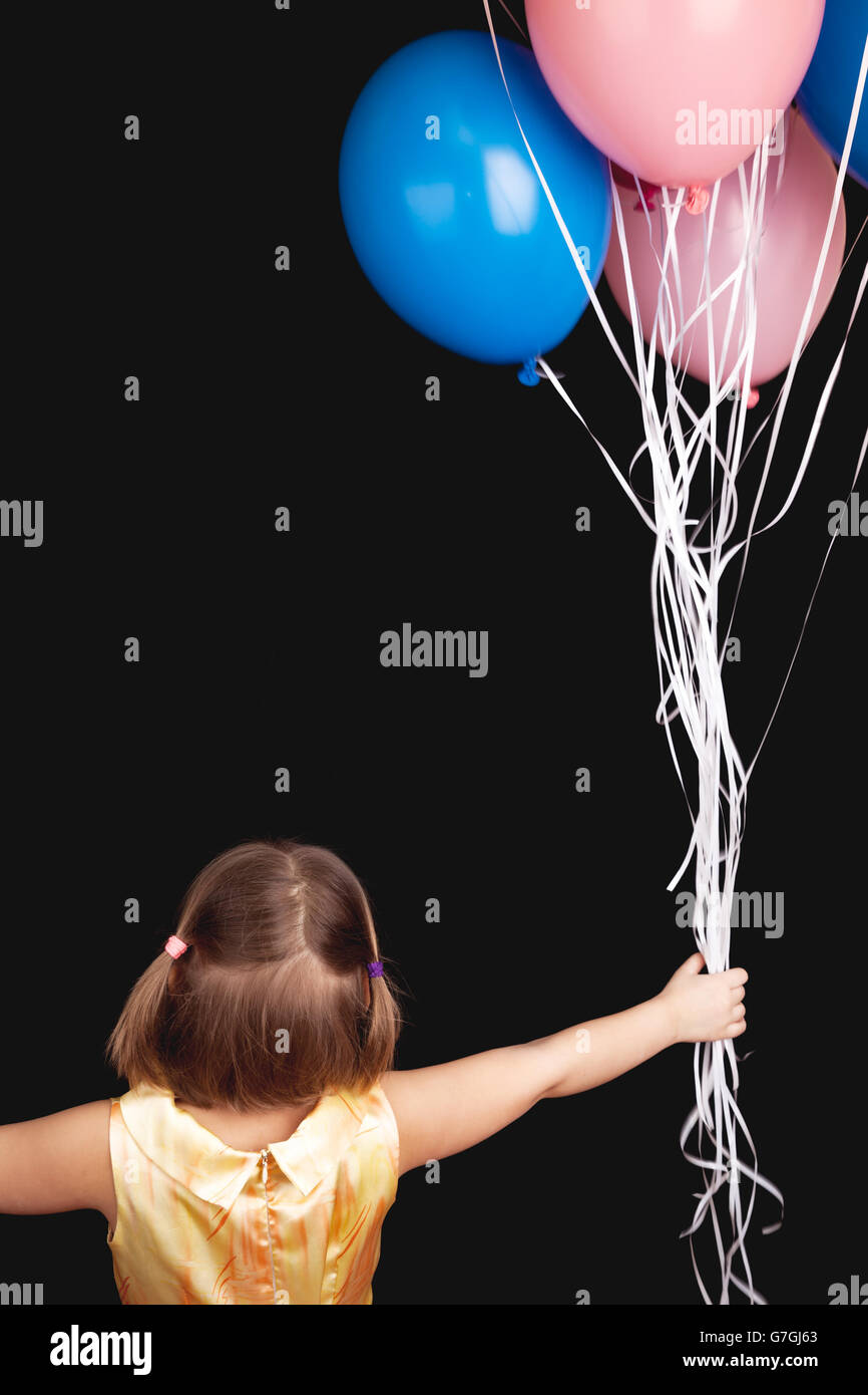 Caucasian blond little girl with colorful balloons, rear view over black background Stock Photo