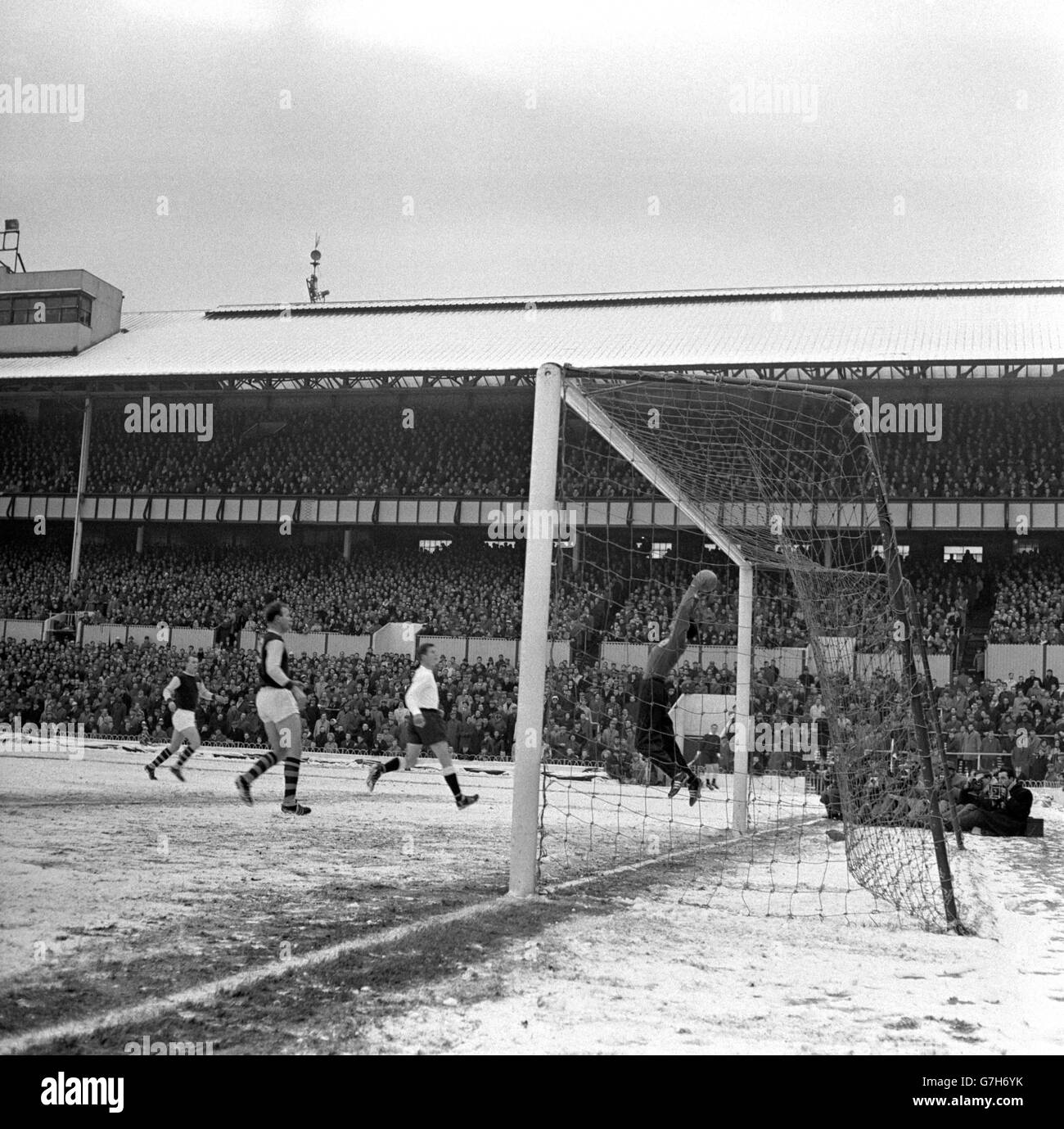 Tottenham Hotspur goalkeeper Bill Brown, wearing a tracksuit against the cold, jumps high and makes a clean save watched by Burnley centre-forward Andy Lochhead (second from left) during the delayed FA Cup third round tie in the snow at White Hart Lane. The match kicked off early at 2.15pm due to the advice of the local Electricity Board office, in light of the current power difficulties. Stock Photo