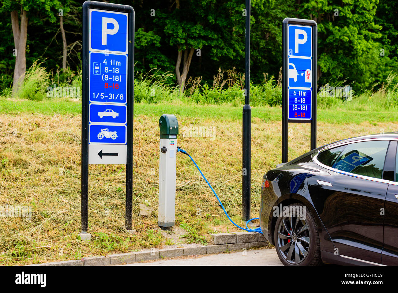 Soderkoping, Sweden - June 20, 2016: Public charge station for electric cars in use by black Tesla car. Traffic signs tells abou Stock Photo