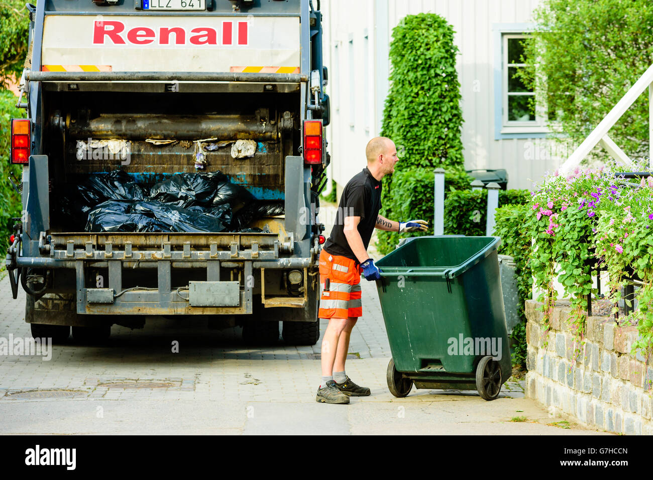 Soderkoping, Sweden - June 20, 2016: Male garbage collector rolling an empty trash bin back to a house in the neighborhood. Garb Stock Photo