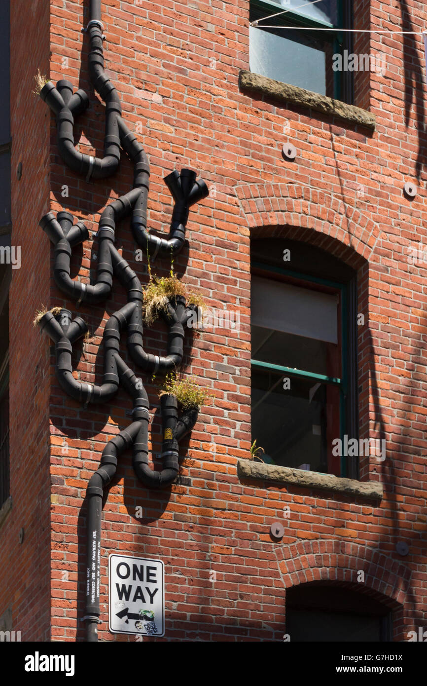 black rain gutter pipes fixed in an intricate and unusual way to a red-brown brick wall Stock Photo