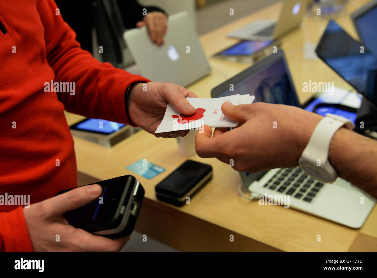 An Apple employee hands-out a red Apple sticker following a purchase as the Apple store on Regent Street, London, displays red logos in recognition of World AIDS Day as Apple stores across the globe go red, with a red logo and other red elements in store. Stock Photo