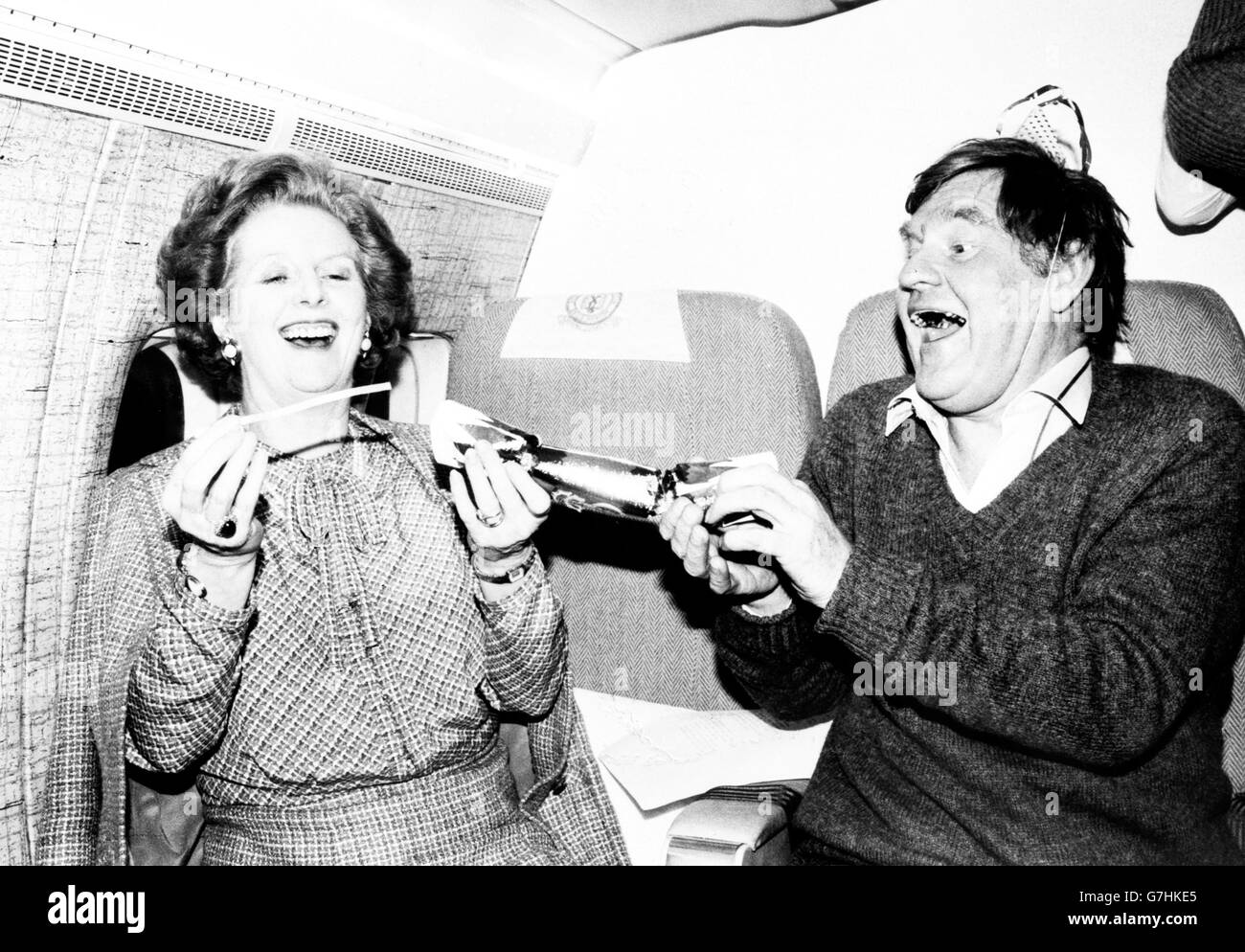 Prime Minister Margaret Thatcher pulls a Christmas cracker with her Chief Press Officer Bernard Ingham on the VC-10 taking her from Washington to London. It was the last leg of her round-the-world diplomatic trip. Stock Photo