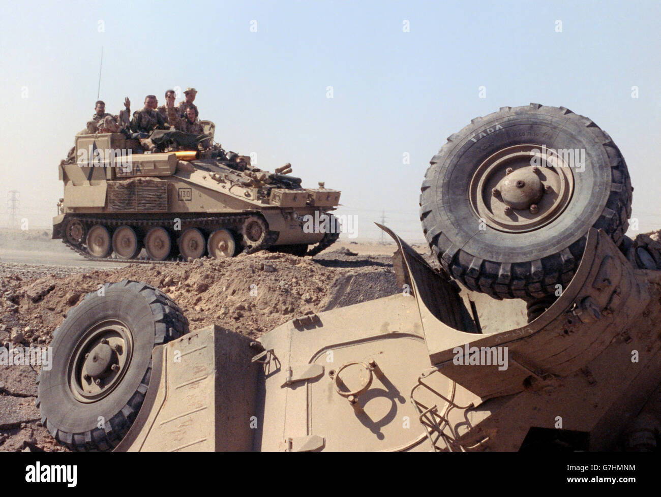 British soldiers riding on an armored personnel carrier pass a destroyed Iraqi APC in the desert following the liberation of Kuwait in Operation Desert Storm February 27, 1991 outside Kuwait City, Kuwait. Stock Photo
