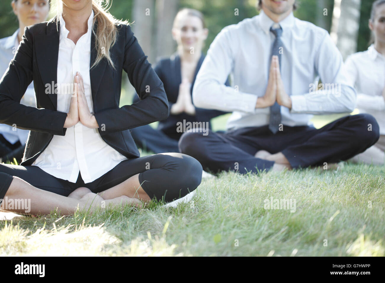 Business people practicing yoga in park Stock Photo