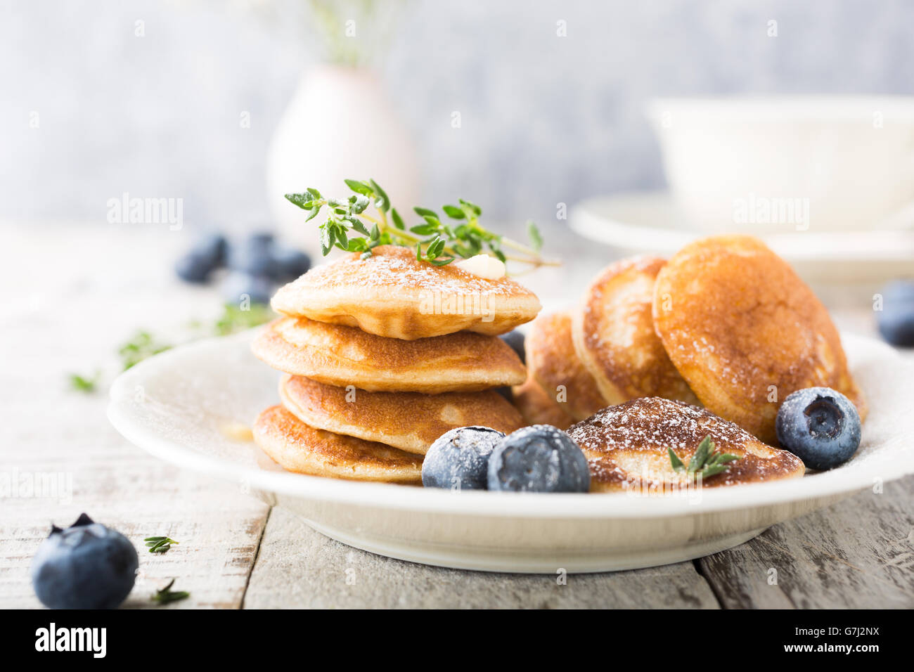 Dutch mini pancakes called poffertjes with blueberries and thyme, sprinkled with powdered sugar. Healthy food concept. Stock Photo