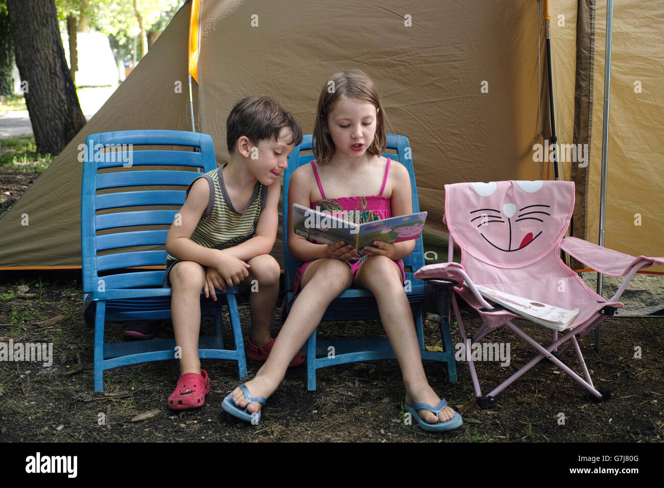 Lago di Bracciano. Lazio. Italy. Six year old girl reading to a younger 4 year old boy on camping holiday. Stock Photo