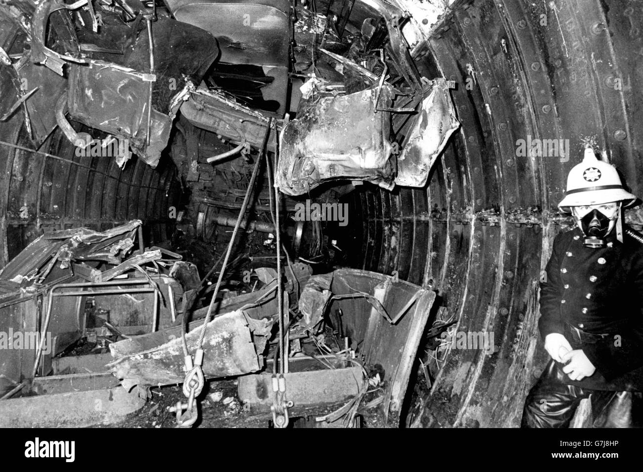 Squashed against the roof of the Tube tunnel at Moorgate is the first coach of the train that smashed into the tunnel wall. Amid the wreckage are the front bogie wheels from the second coach. The foul air forces the fireman to wear a breathing mask. Stock Photo