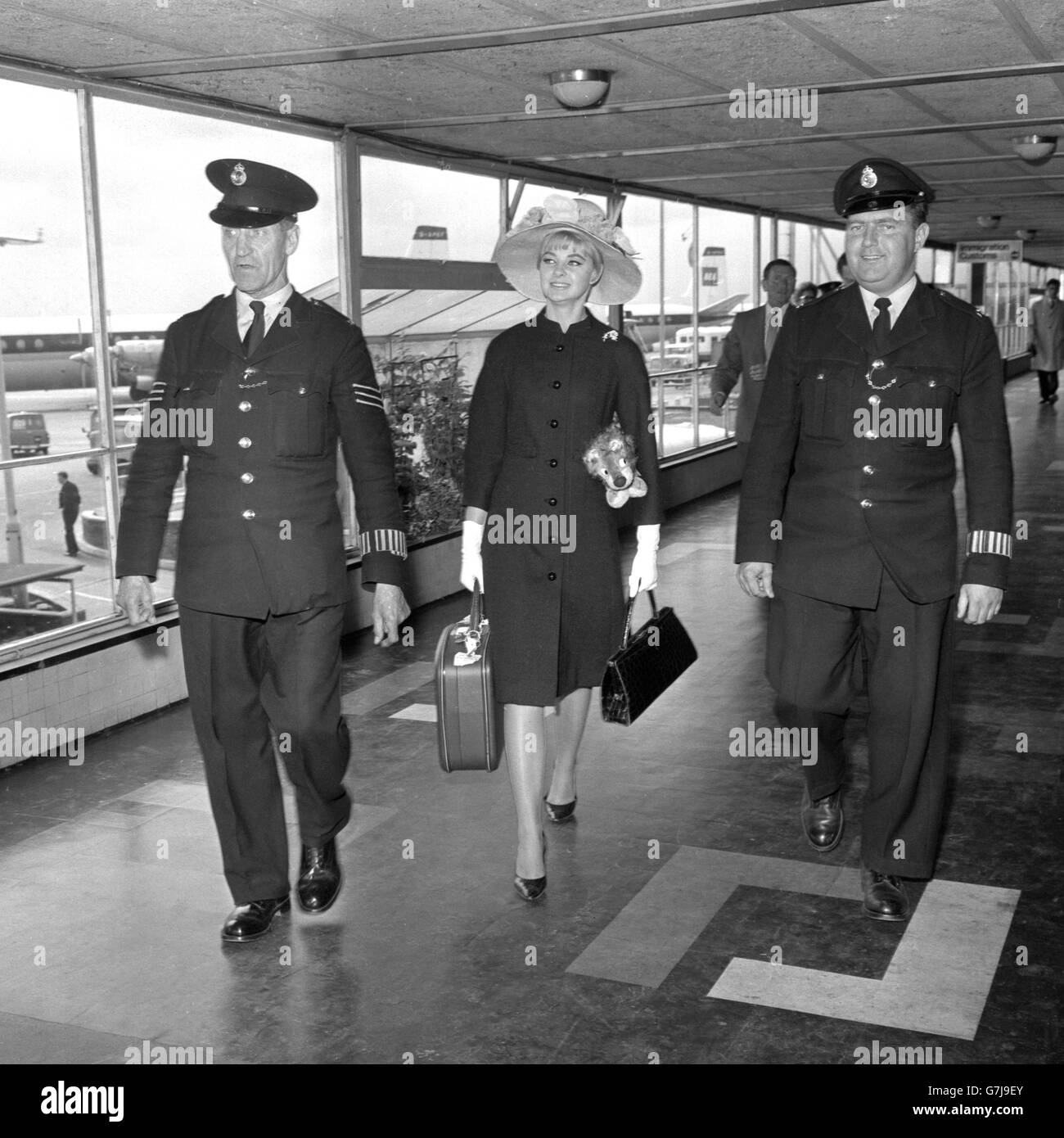 Escorted by two airport policemen, Marilyn (Mandy) Rice-Davies, 18-year-old witness in the Stephen Ward case, walks to the plane when she leaves London Airport for Palma, Majorca. Stock Photo