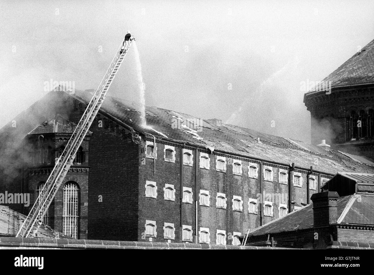 High above Manchester's burning Strangeways prison, a lone fireman battles to put out the dawn fires started by rioters. The six remaining prisoners lit the fires after authorities kept them awake with spotlights, firecrackers and sprayed water from fire hoses on the building. Stock Photo