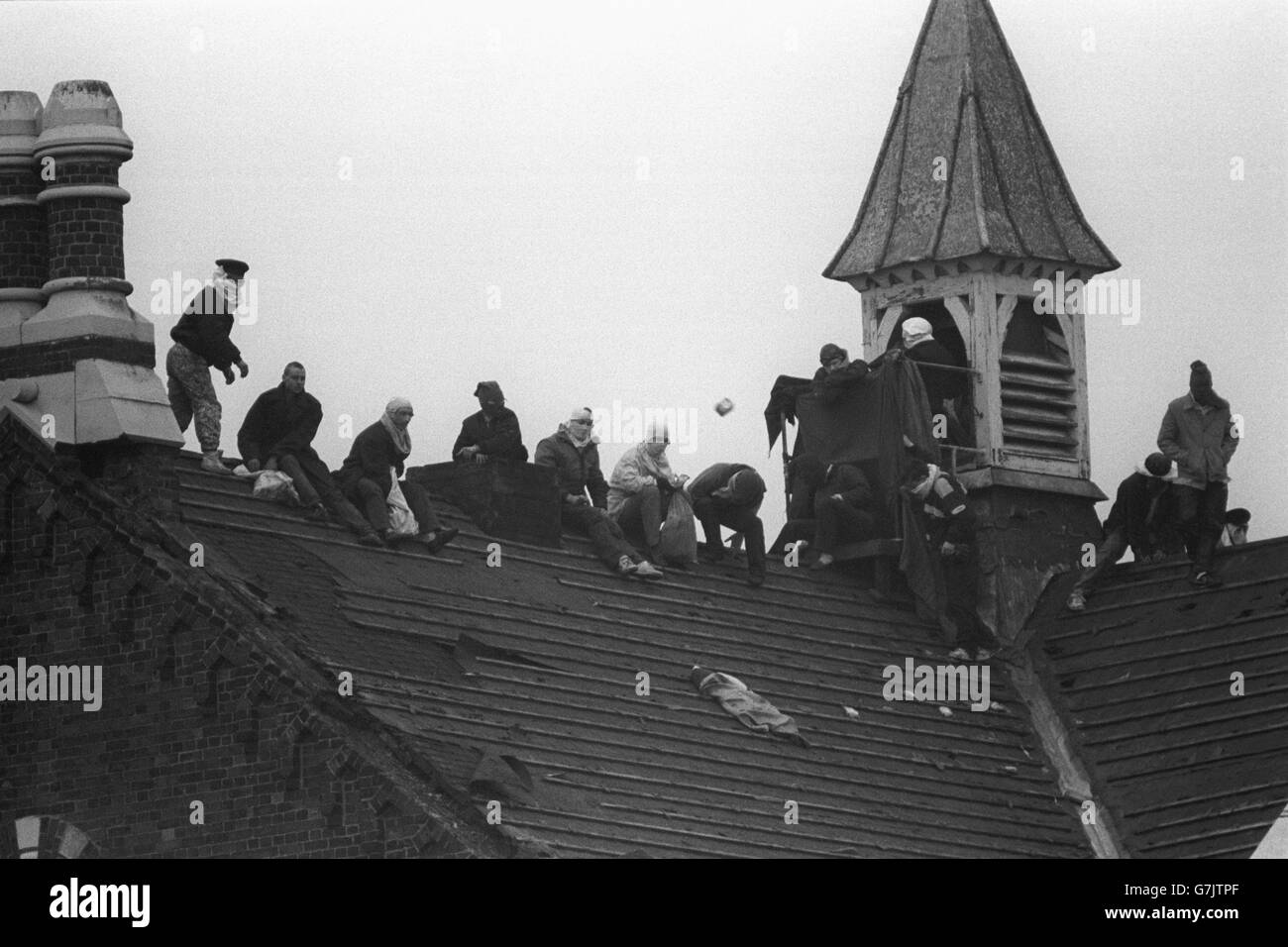 Prisoners continue their rooftop protest, with one of the prisoner's (l) throwing bricks into the Strangeways prison yard. Stock Photo