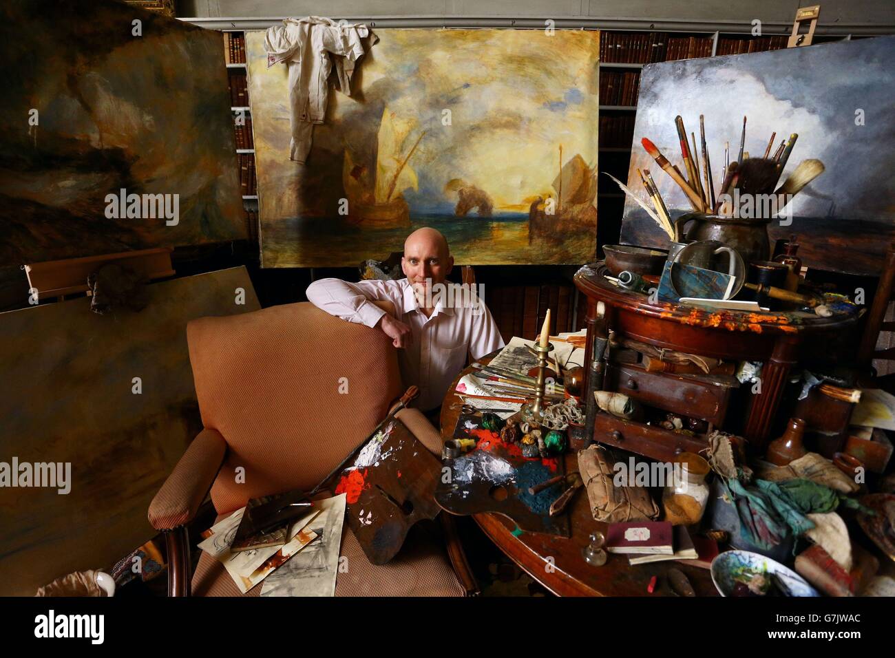 Andrew Loukes, Curator of Collections and Exhibitions at Petworth House in West Sussex, sits amongst a re-creation of a studio used by the artist JMW Turner which has been created from studio props used in the shooting of the film Mr. Turner ahead of an exhibition at the House which was the home of Turner's patron, Lord Egremont. Stock Photo