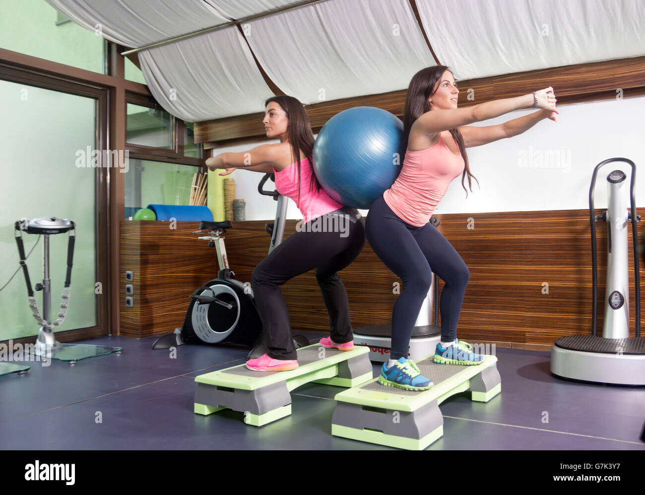 Two women exercise stability ball between backs, stepper, gym. Stock Photo