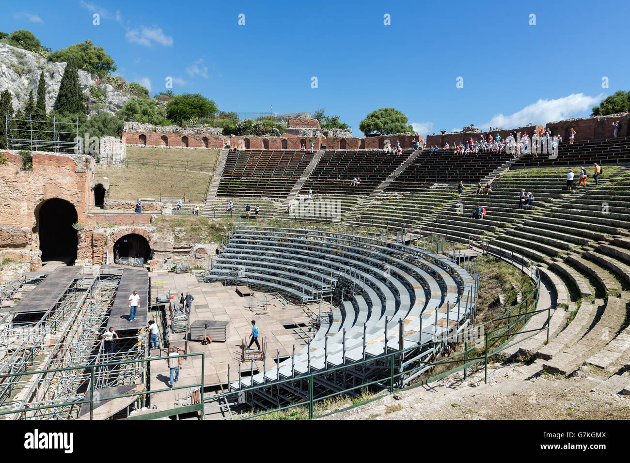 Tourists visiting the ancient Greek theater of Taormina city while workers mounting a stage in