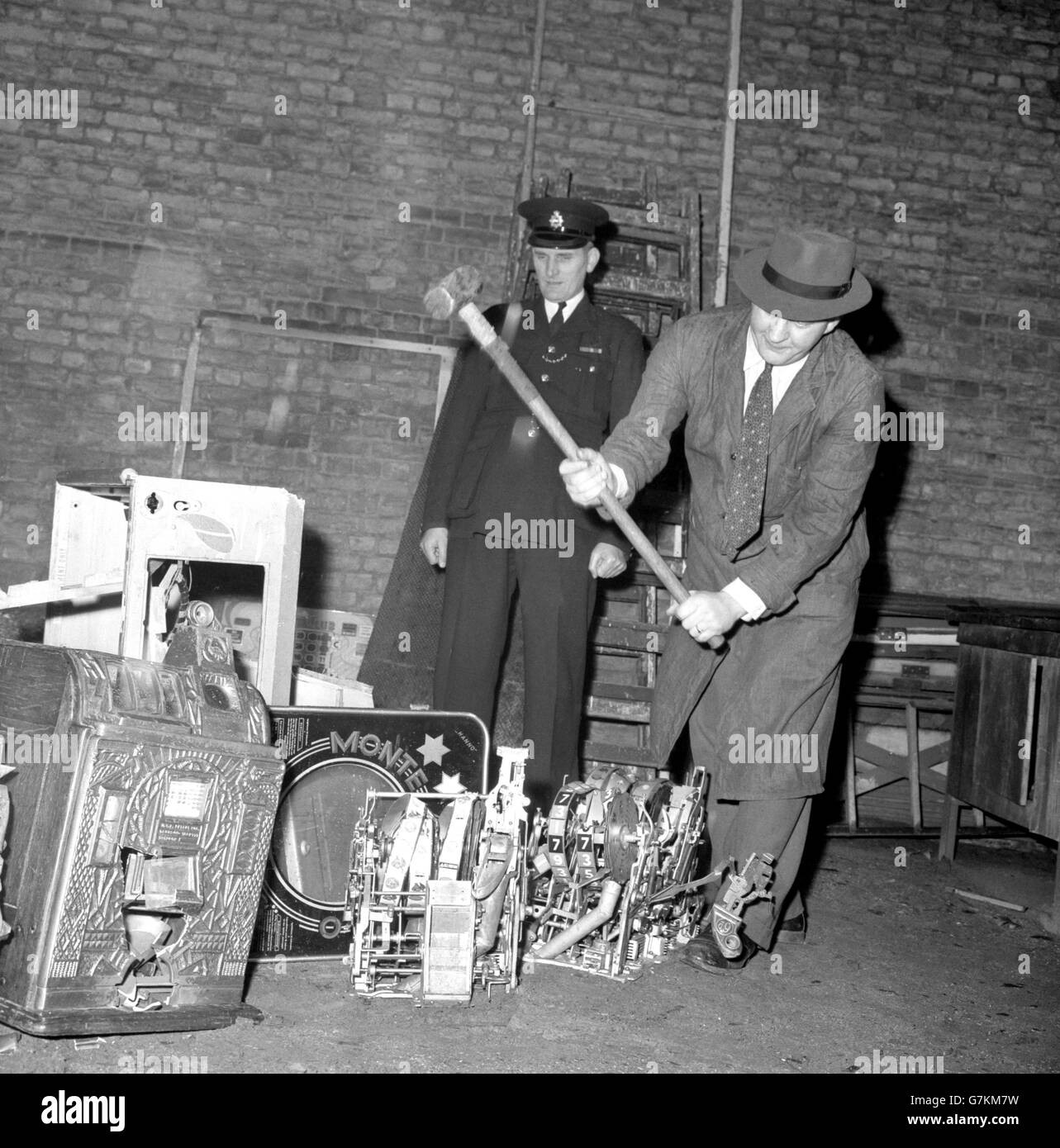 An engineer uses a sledge to destroy fruit machines ('one-armed bandits') and pin tables under the supervision of Inspector George Strachan at New Scotland Yard, London. Later on, they were burned. The machines were the first of 150 ordered to be destroyed after being seized by police in the last four months. Some of these machines were on show last week when the Metropolitan Police Commissioner explained the law relating to gaming machines, which comes into force on January 1st, 1961. Stock Photo