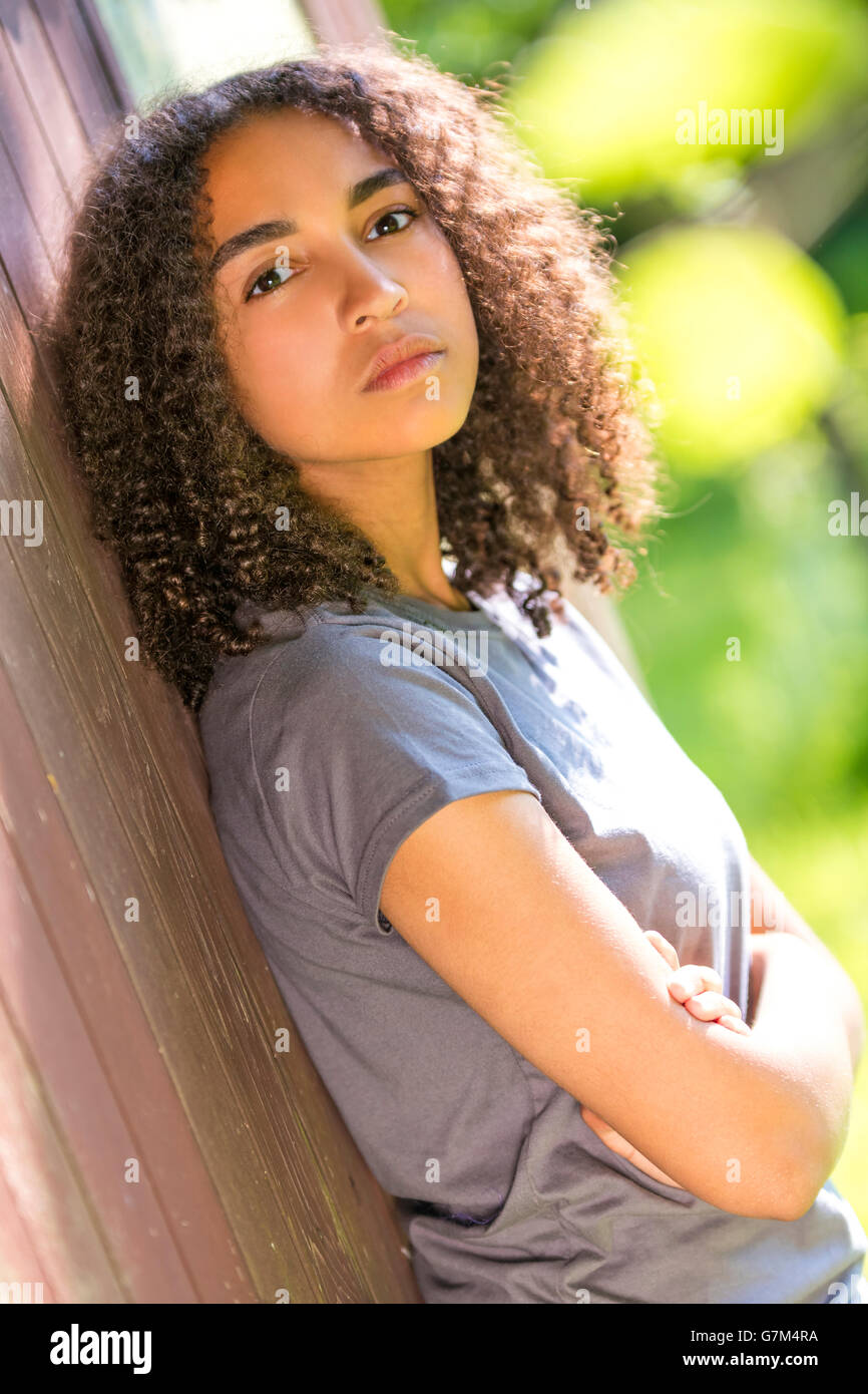 Mixed race African American girl teenager female young woman arms folded in spring or summer looking sad depressed or thoughtful Stock Photo