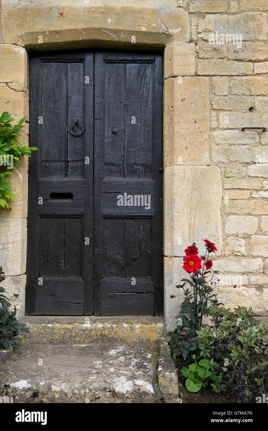 Red dahlia flowers by old black wooden house doors. Chipping campden, Cotswolds, Gloucestershire, England Stock Photo