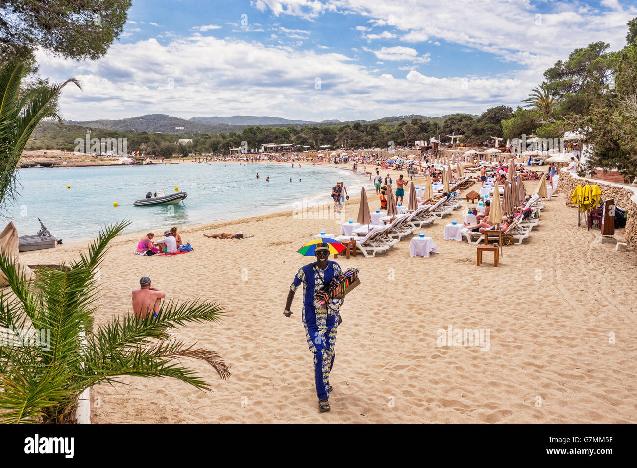 The beach at Cala Bassa, Ibiza, with beach vendor, known as looky looky man, approaching. Stock Photo