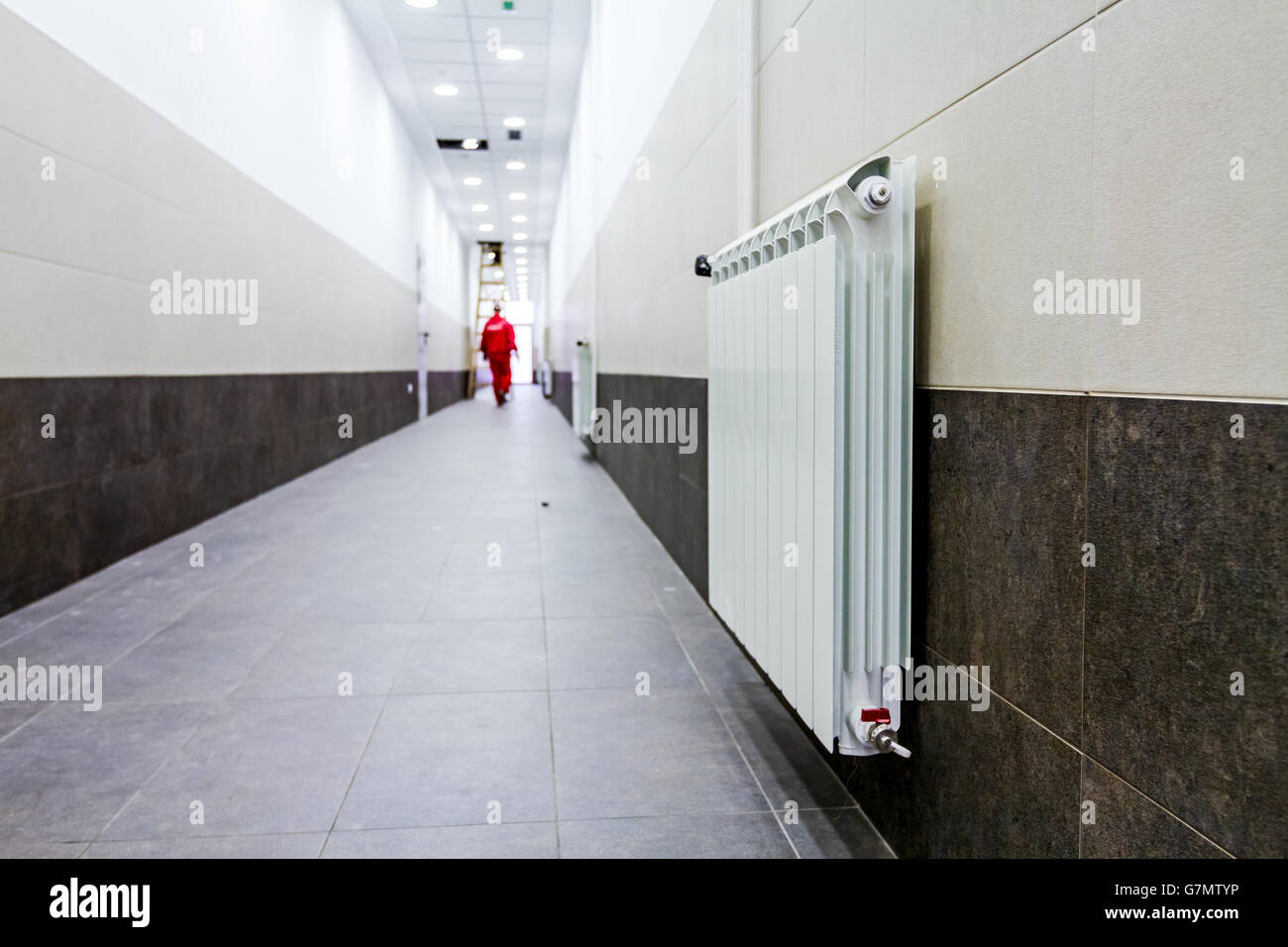White radiator in long narrow corridor with tilled wall and floor Stock