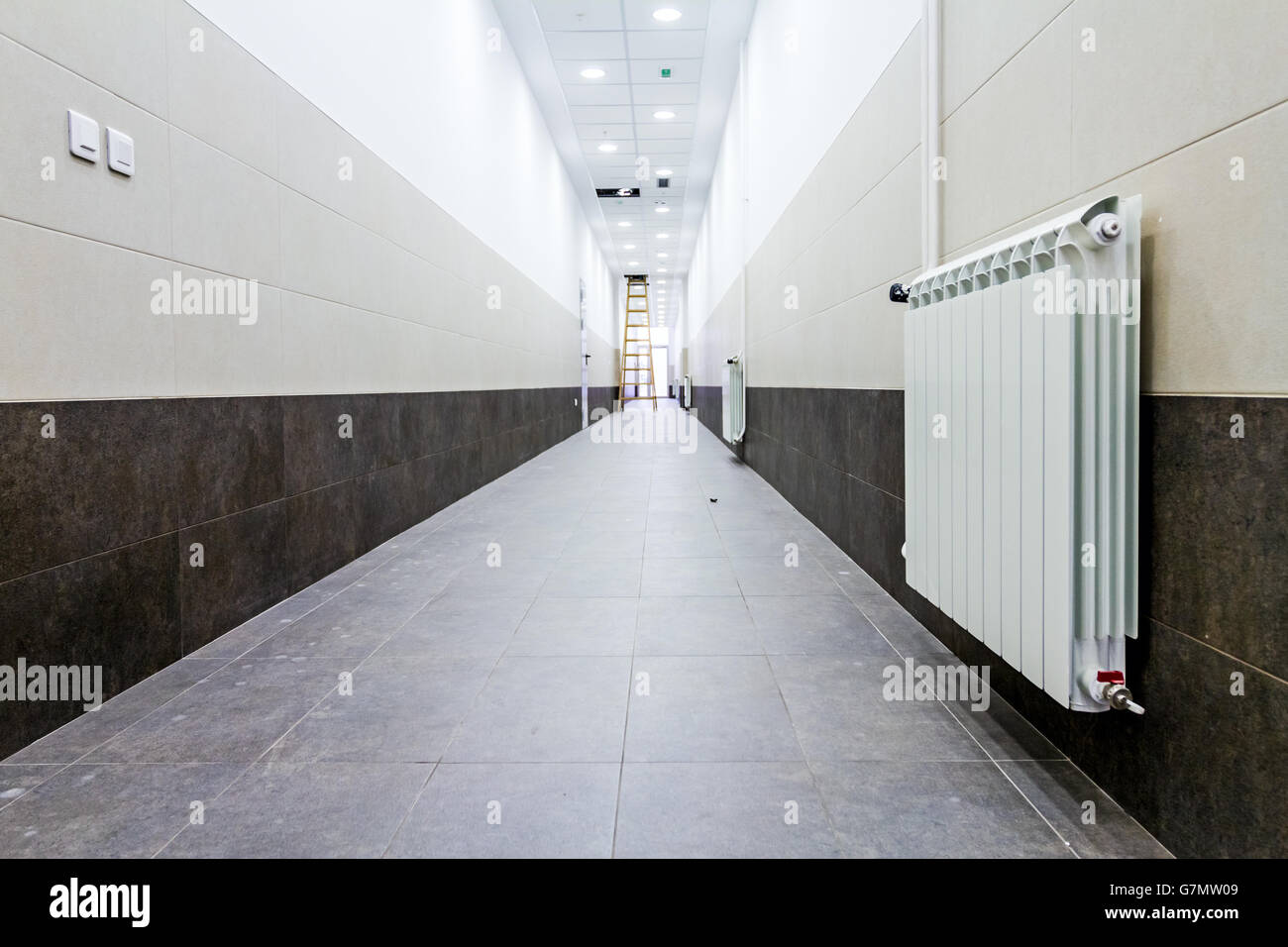 White radiator in long narrow corridor with tilled wall and floor Stock