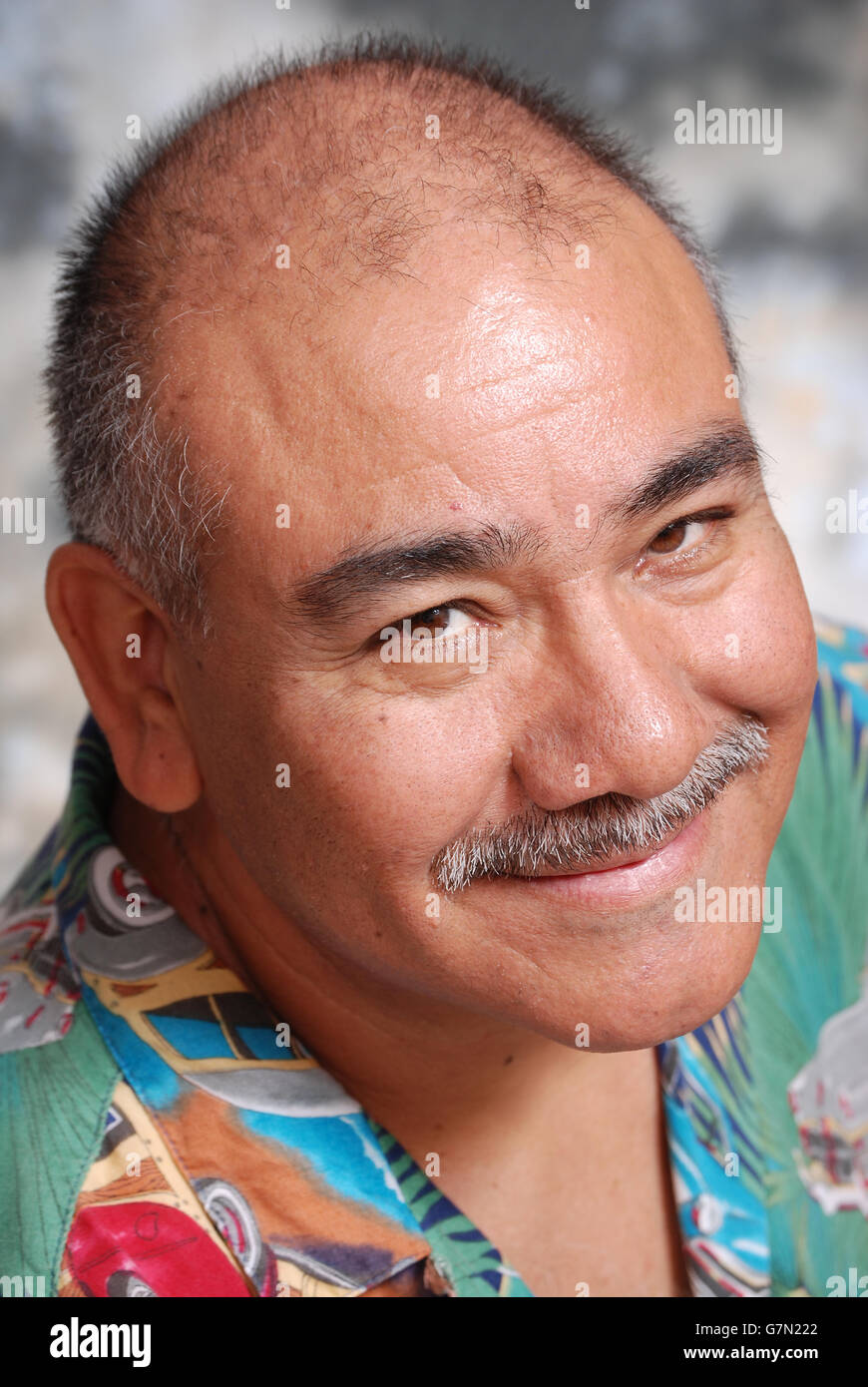Close up portrait of a smiling senior man wearing a colorful shirt against a muddled gray background. The man is Hispanic. Stock Photo