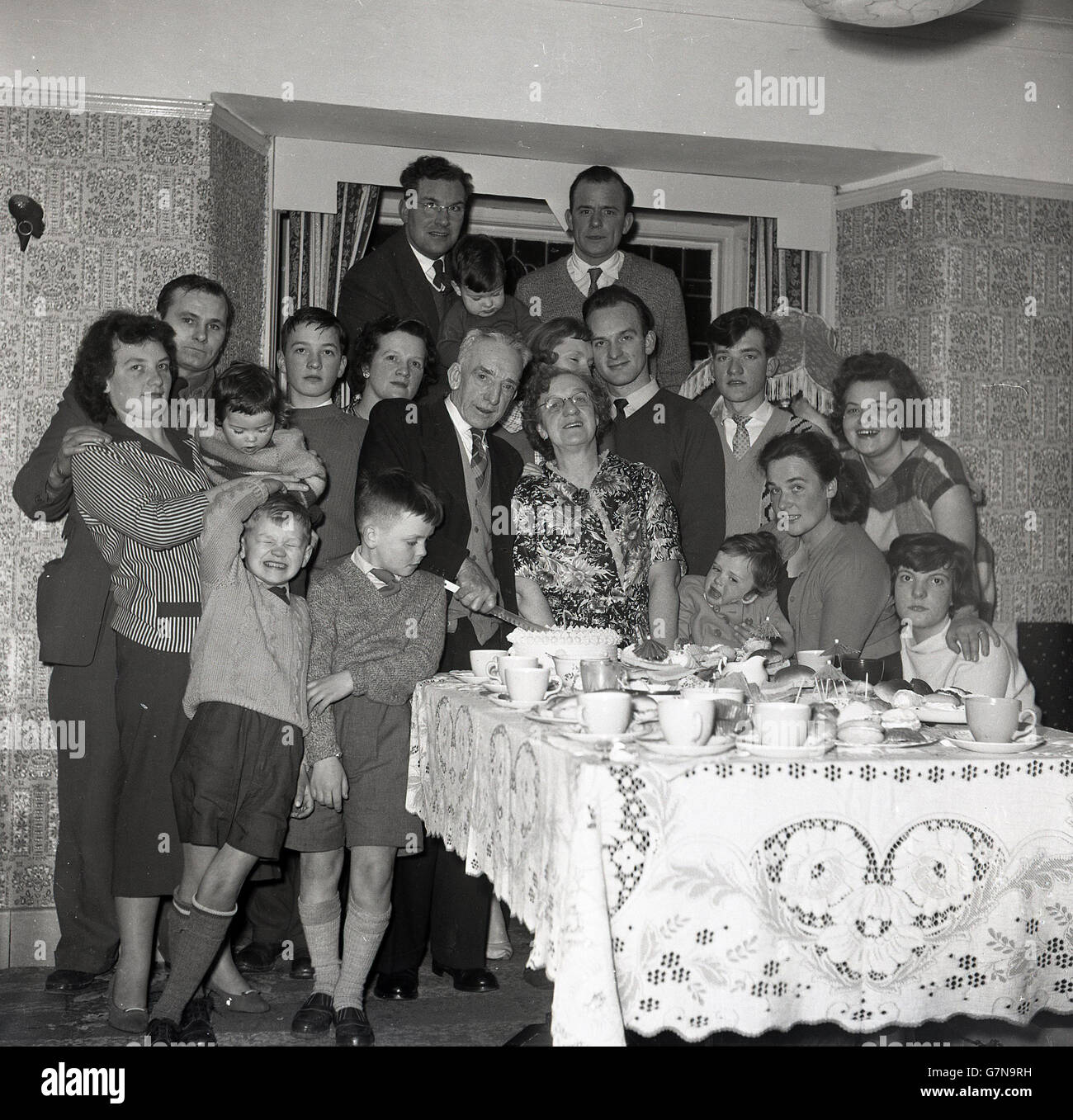 1950s, historical picture, a whole family generation celebrate a grandparents wedding anniversary as they cut the cake. Stock Photo