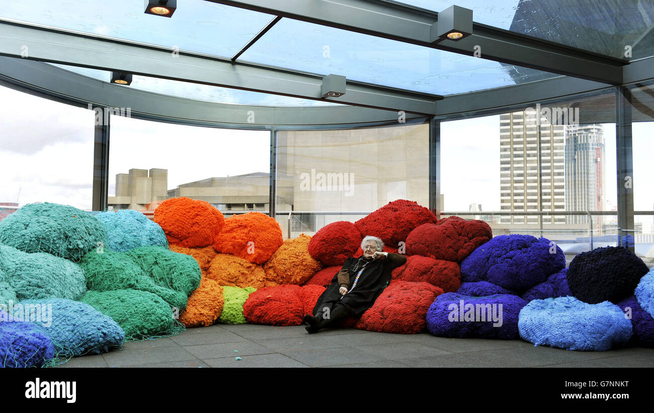 Artist Sheila Hicks, sits on her installation made from large-scale bundles of coloured fabric that visitors are welcome to sit on and interact with, during the preview at the Hayward Gallery, London, of 'Sheila Hicks: Foray into Chromatic Zones' exhibition. Stock Photo