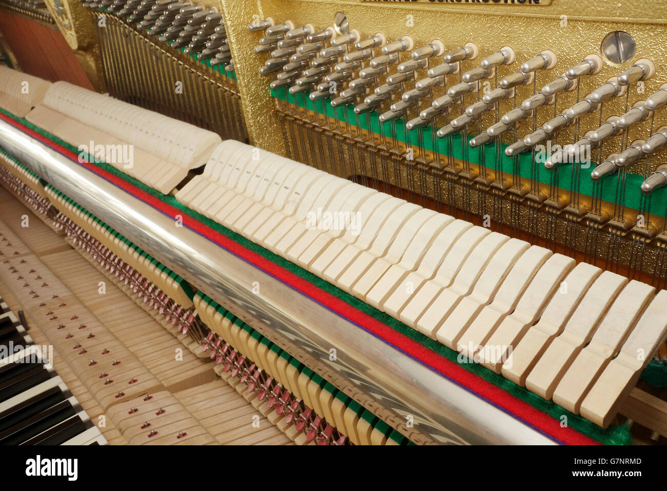 Diagonal view of an upright piano action mechanism. Keyboard, hammer rail, hammers and tuning pins on pin block are in view. Stock Photo
