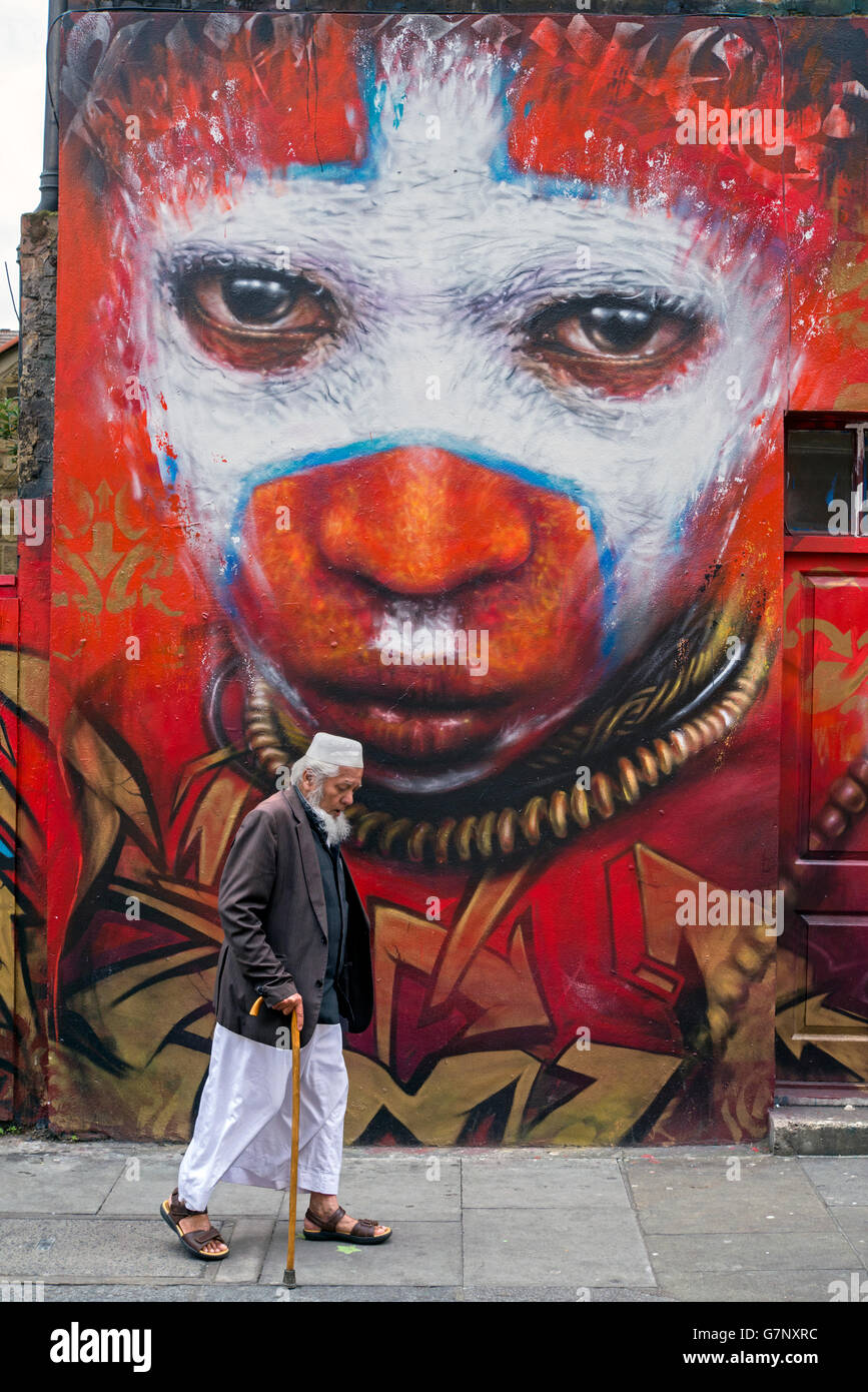 An elderly Asian man walks by a piece of street art by Dale Grimshaw in Hanbury Street, just off Brick Lane, London. Stock Photo