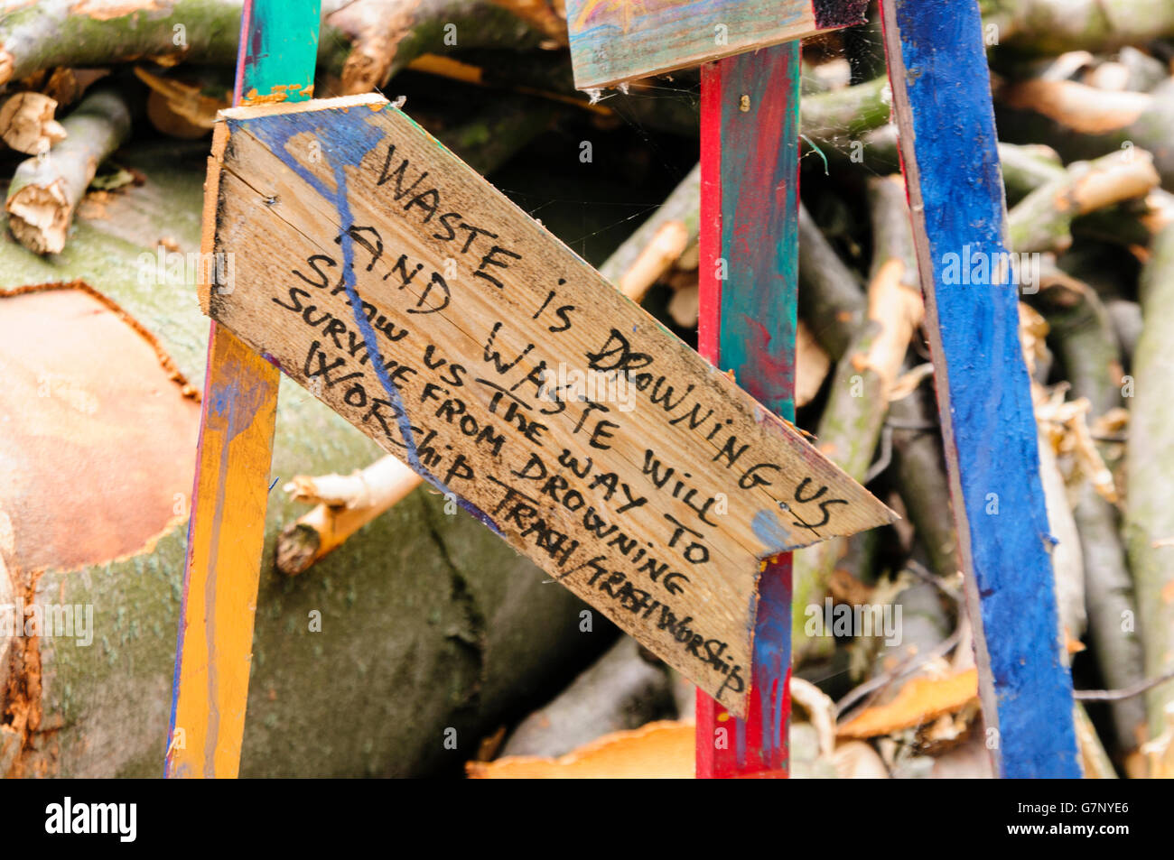 Sign saying 'Waste is drowning us and waste will show us the way to survive from drowning. Worship trash/trash worship.' beside a pile of wooden logs. Stock Photo